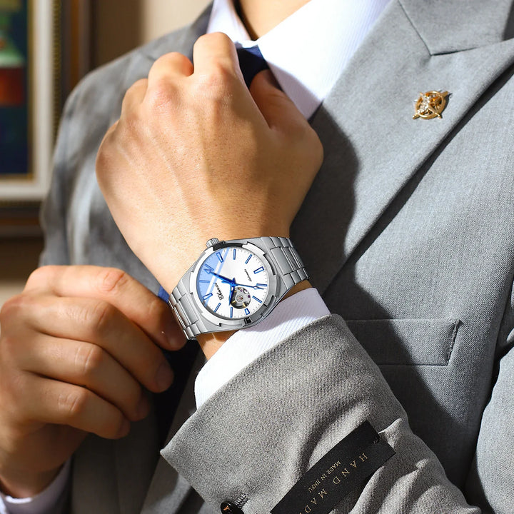 Close-up of man adjusting navy blue tie wearing silver wristwatch with white dial and blue hands in gray suit