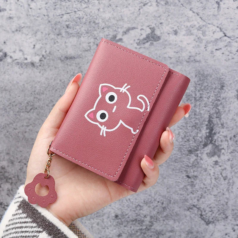 Hand holding pink leather wallet with cute cartoon cat and flower charm against gray textured background