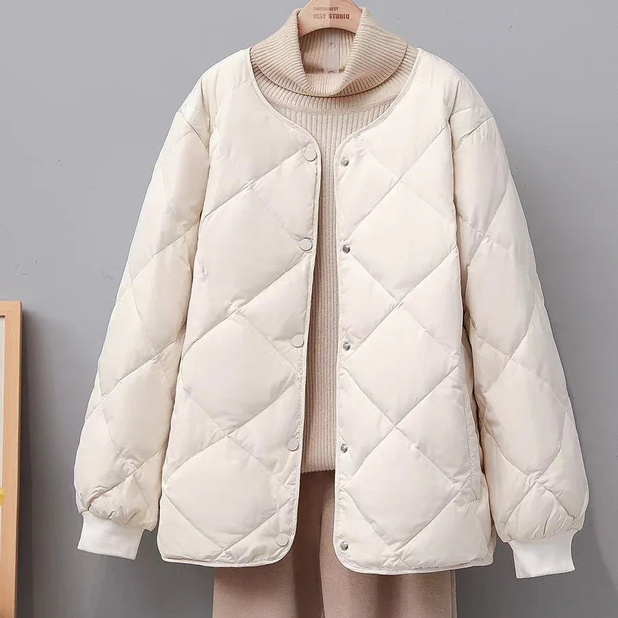 Cream quilted puffer jacket with snap buttons on beige turtleneck sweater and pants against gray background