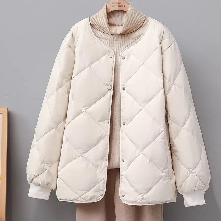 Cream quilted puffer jacket with snap buttons on beige turtleneck sweater and pants against gray background