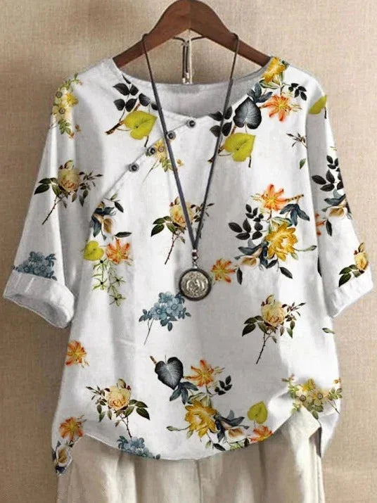 White floral blouse with yellow, orange, blue flowers and green leaves, paired with a pendant necklace
