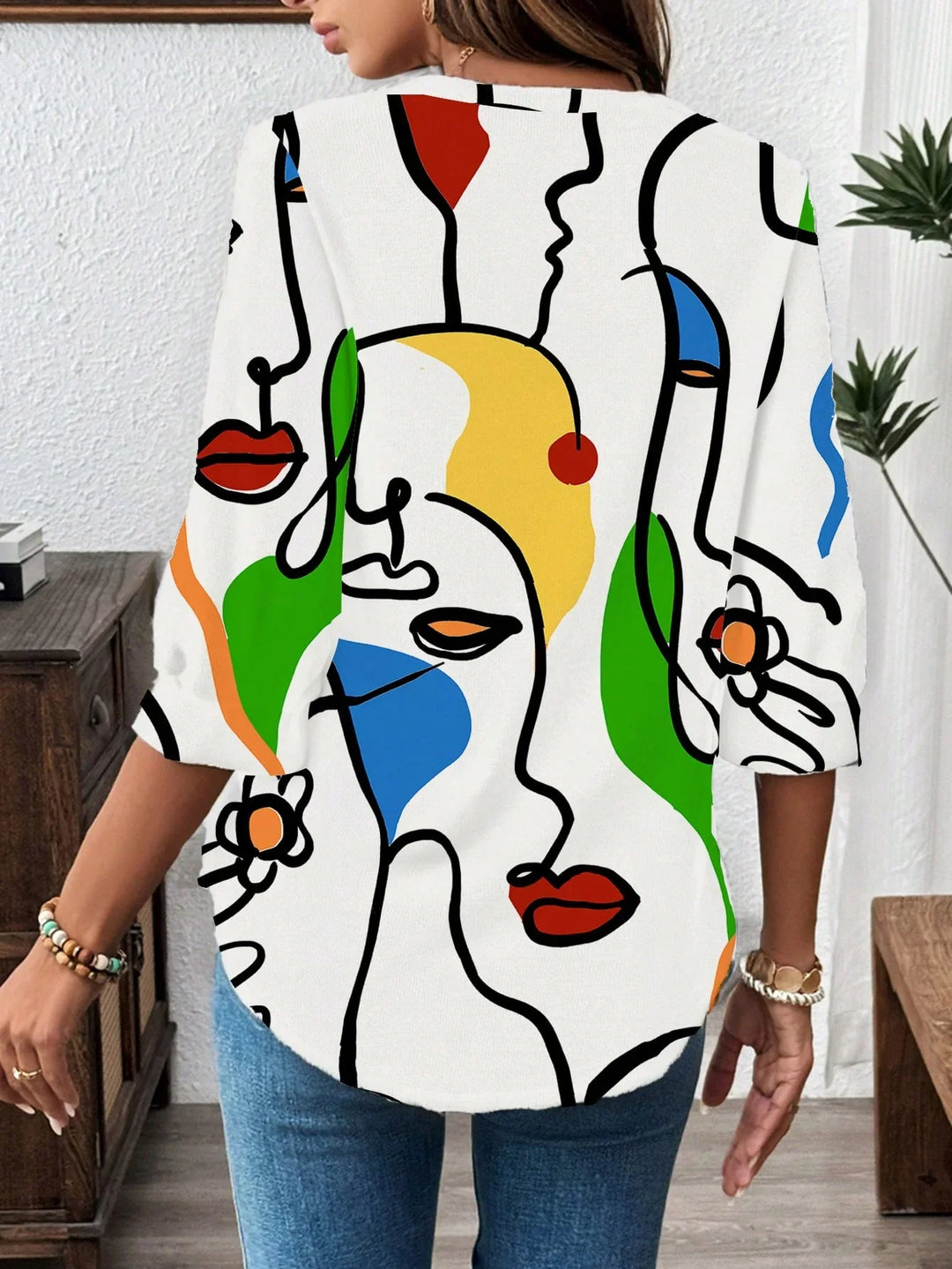 Woman wearing white abstract art print shirt with colorful face line drawings and 3/4 sleeves