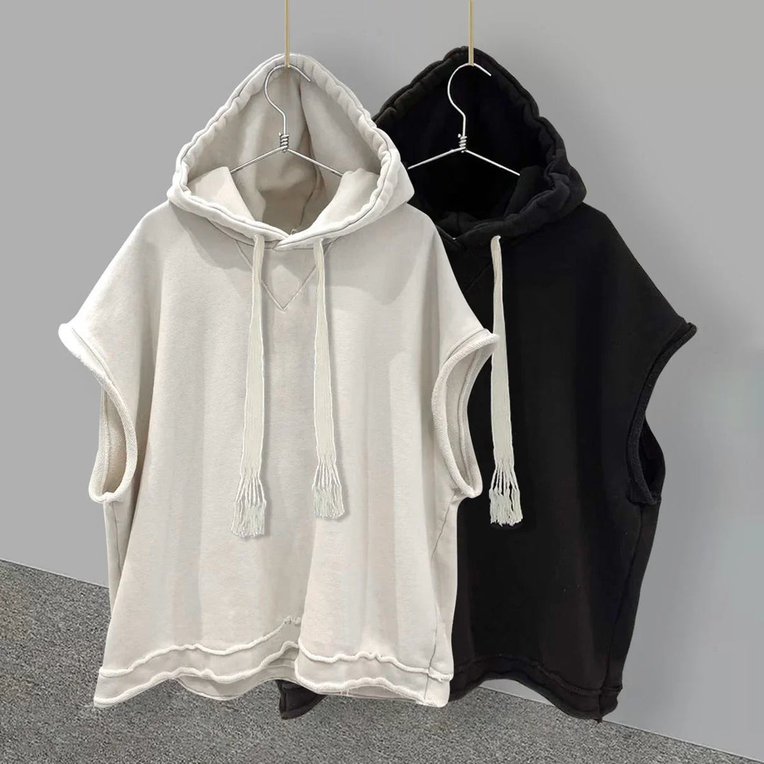 Sleeveless hooded sweatshirts in beige and black with drawstrings, hanging on hangers against gray wall