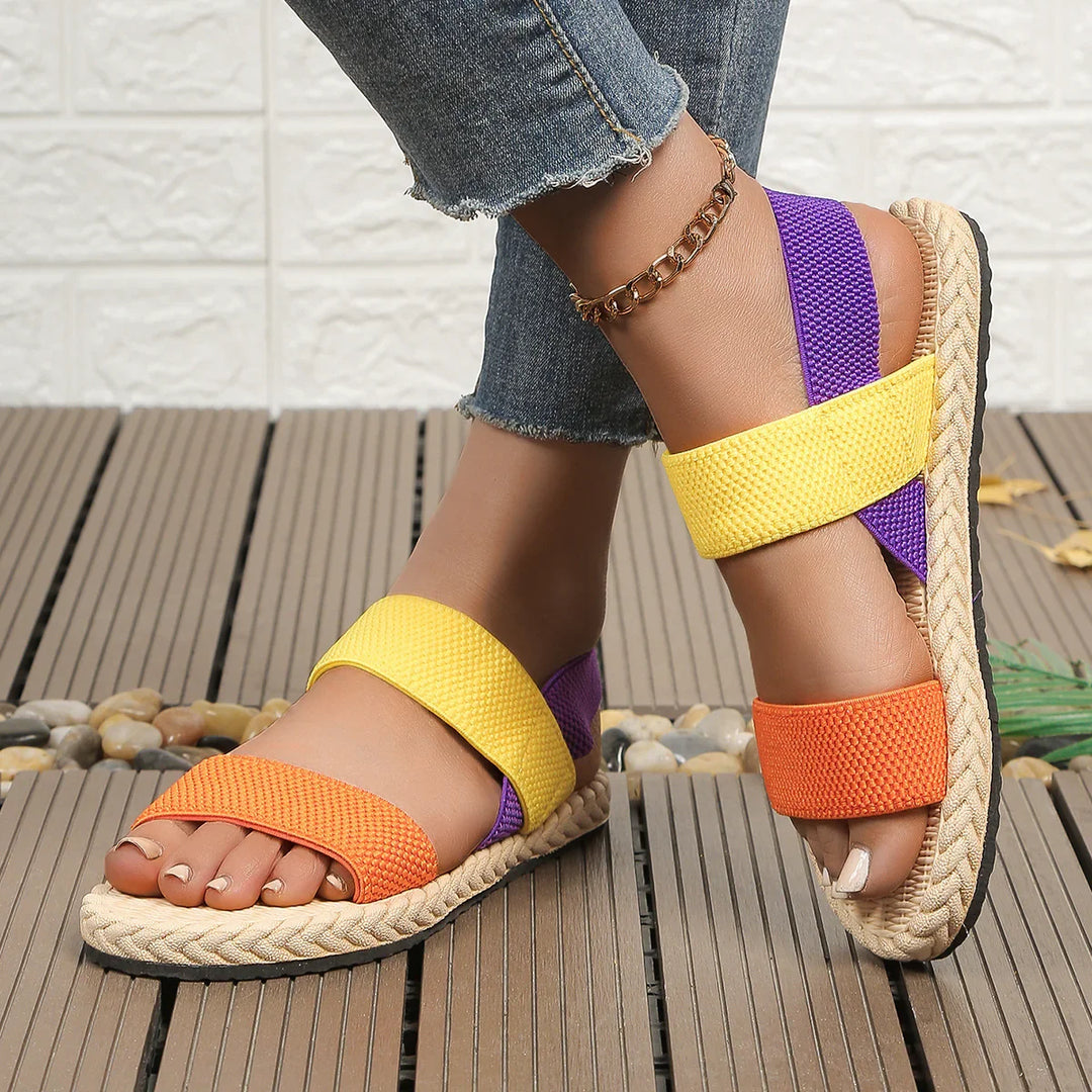 Woman wearing colorful orange, yellow, and purple casual sandals with braided sole and gold anklet