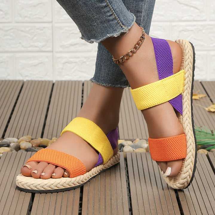 Woman wearing colorful orange, yellow, and purple casual sandals with braided sole and gold anklet