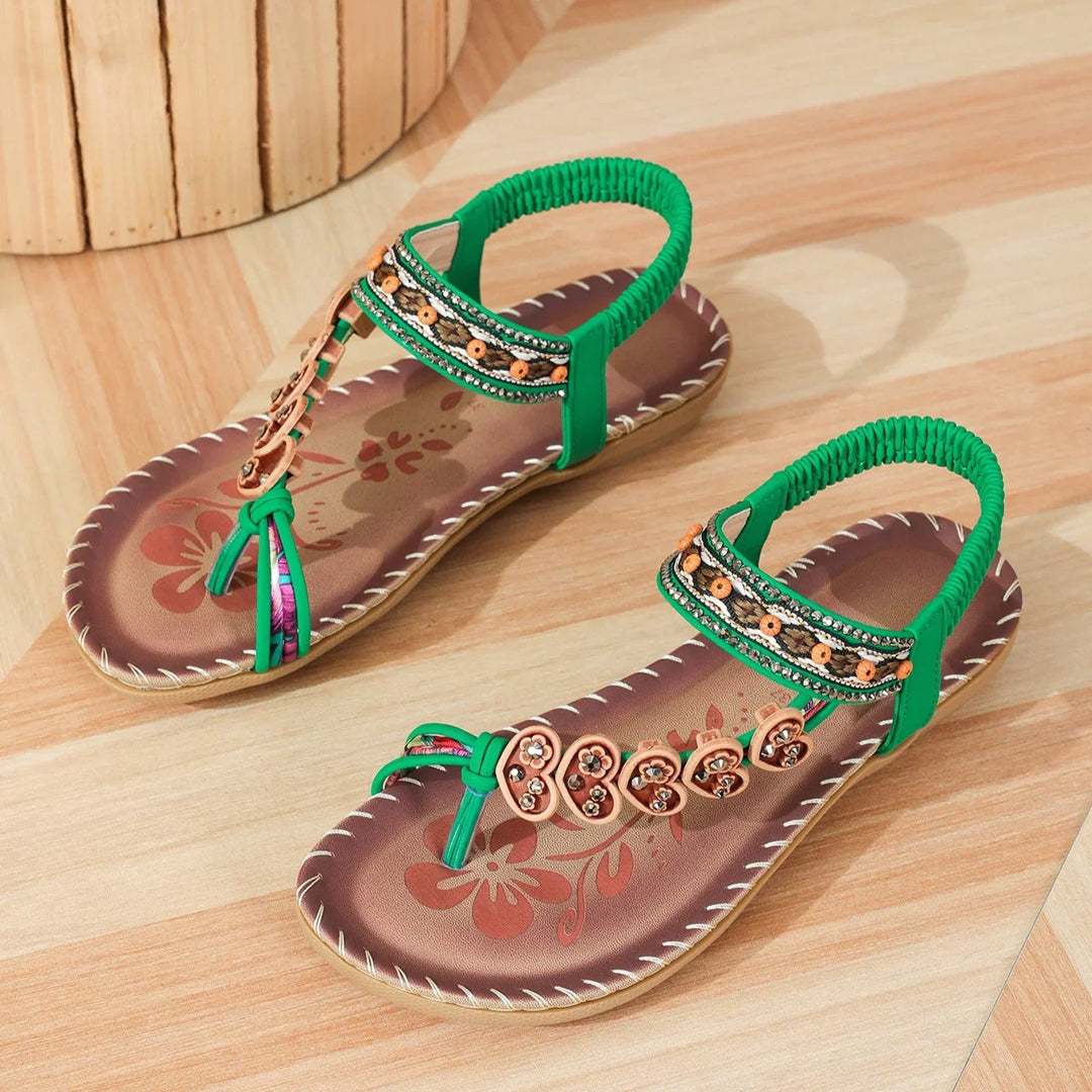 brown and green flat sandals with floral design and beaded embellishments on wooden floor