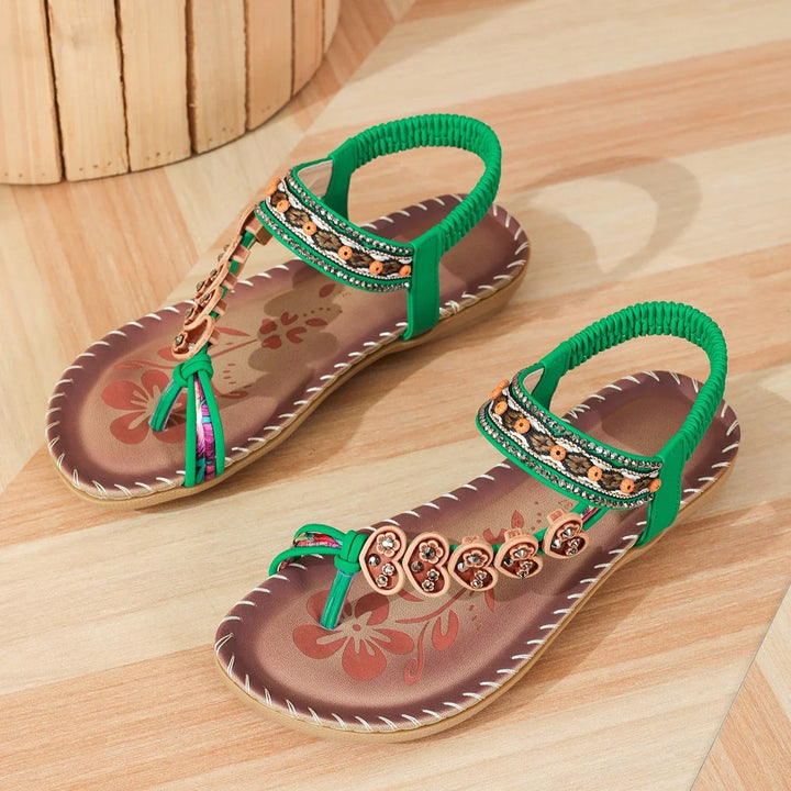 brown and green flat sandals with floral design and beaded embellishments on wooden floor