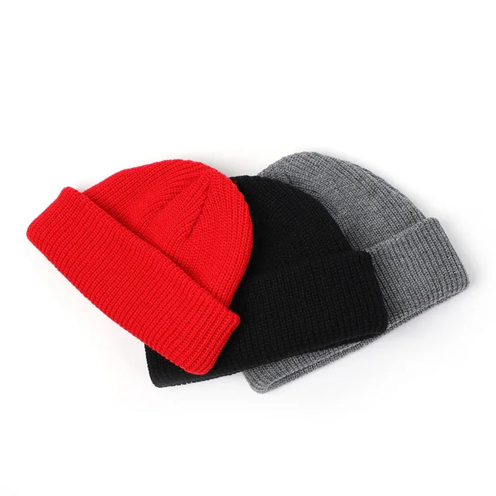 Three folded knit beanies in red, black, and gray on a white background