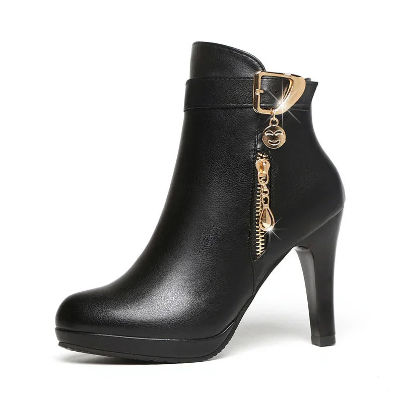 Black high-heeled ankle boot with gold zipper and buckle charm on white background