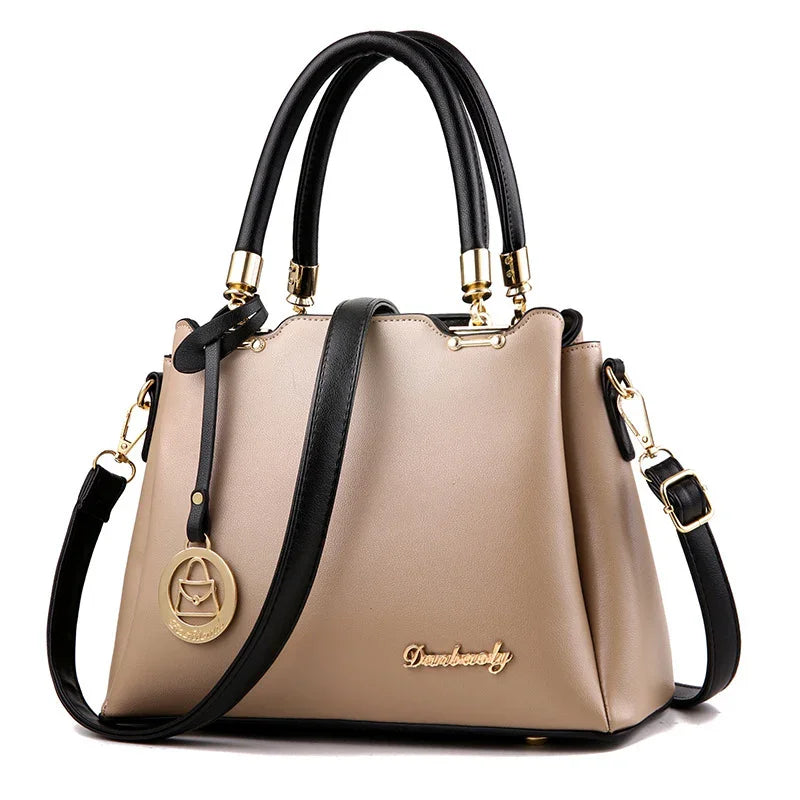 Beige handbag with black handles, detachable shoulder strap, gold hardware, and decorative pendant