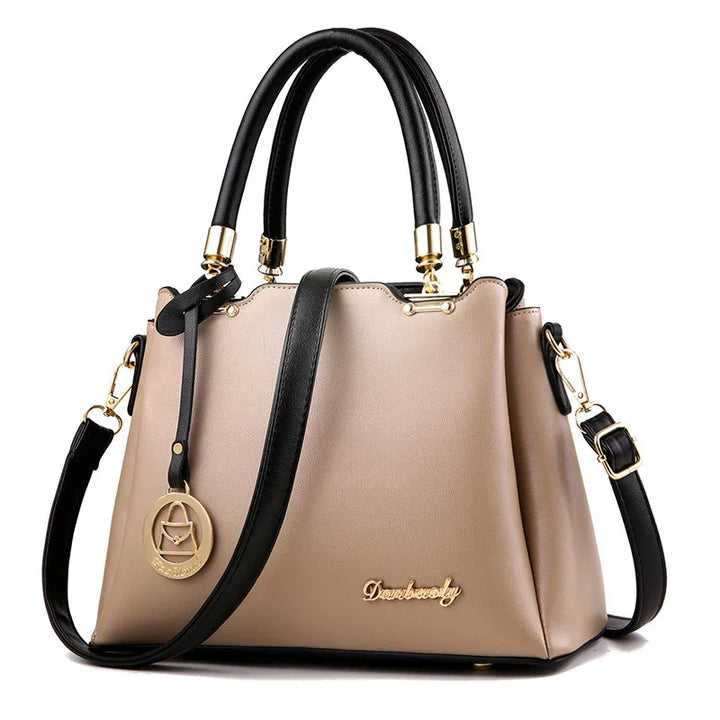 Beige handbag with black handles, detachable shoulder strap, gold hardware, and decorative pendant