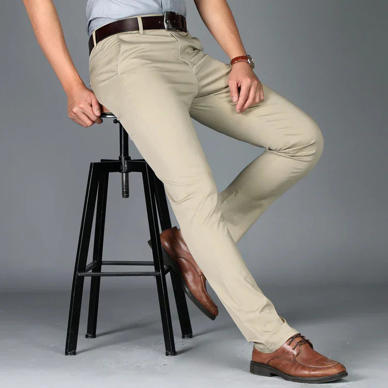 Man wearing beige chinos, brown leather belt, and brown dress shoes sitting on black metal stool