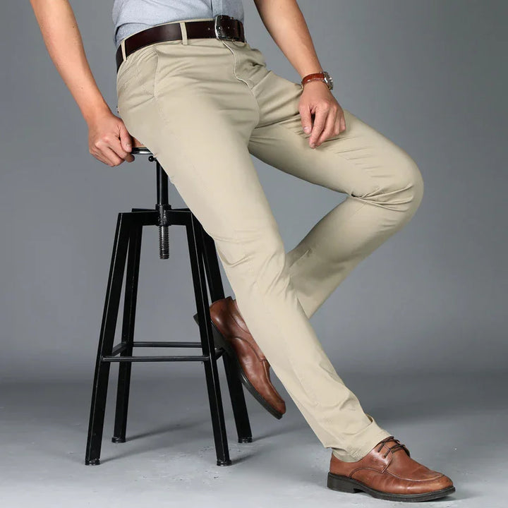 Man wearing beige chinos, brown leather belt, and brown dress shoes sitting on black metal stool