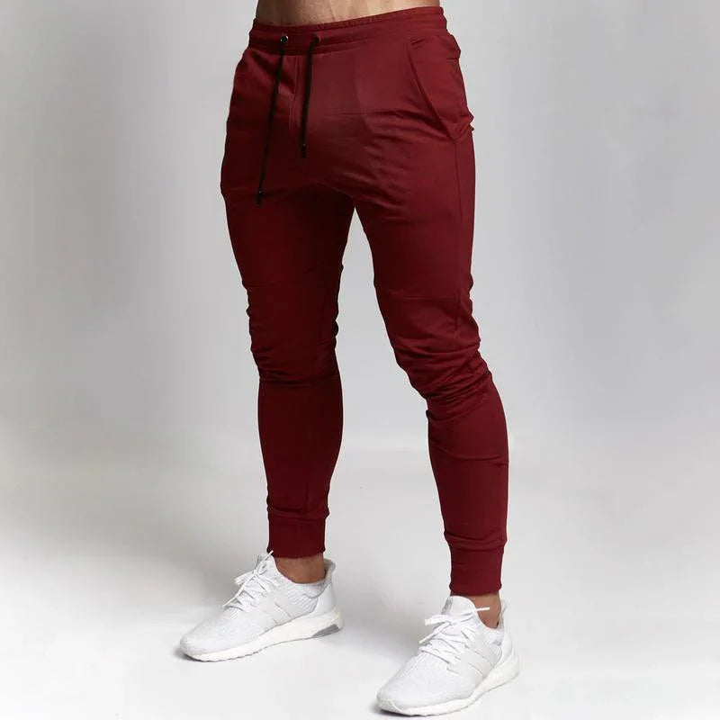 Men's slim fit maroon jogger pants with black drawstring, paired with white sneakers on a white background