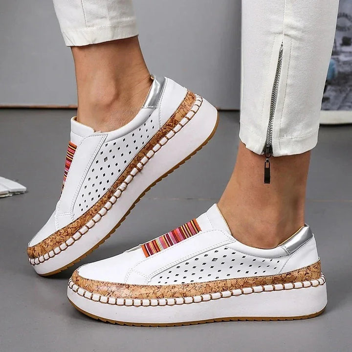 White slip-on platform sneakers with perforated sides and cork accents worn with white pants