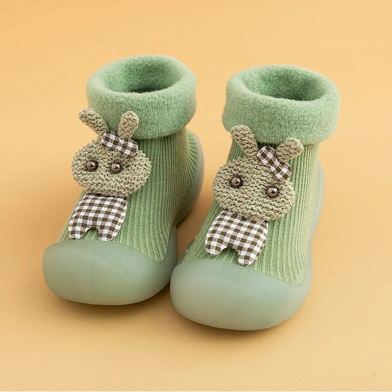 Soft green baby sock shoes with rubber soles and cute bunny applique on beige background