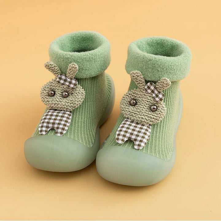 Soft green baby sock shoes with rubber soles and cute bunny applique on beige background