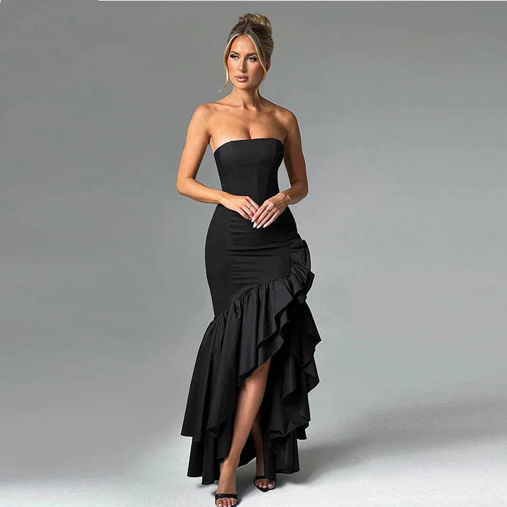 Elegant woman wearing strapless black high-low ruffle evening gown with heels on gray background