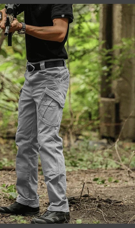 Man wearing gray tactical cargo pants and black shoes standing in a forest setting