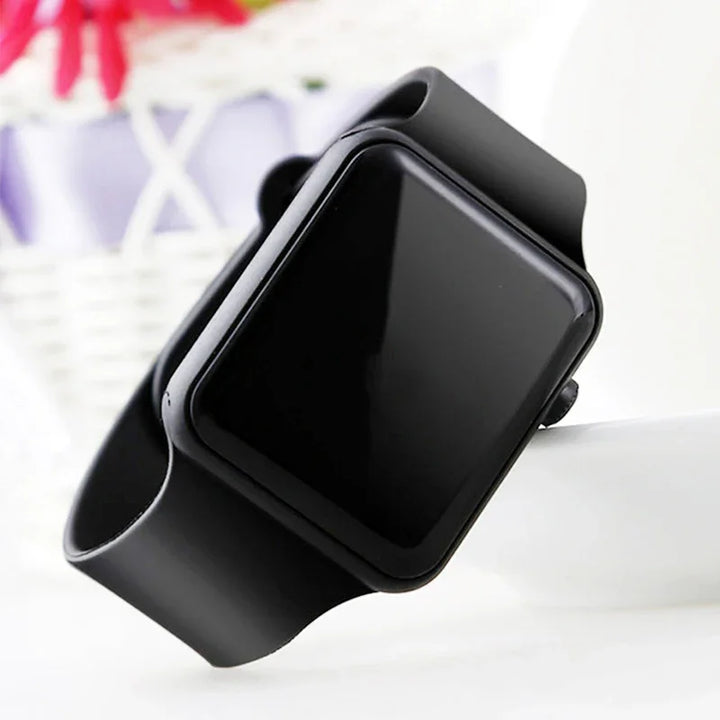 Black smart watch with silicone band displayed on a white surface with blurred background