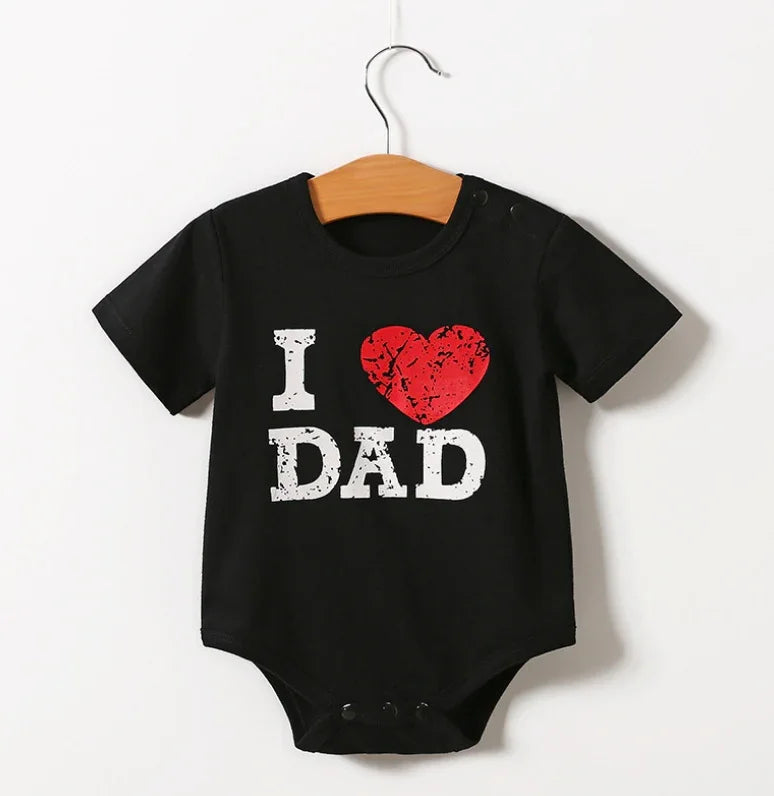 Black baby onesie with distressed white text I love Dad and red heart graphic hanging on wooden hanger