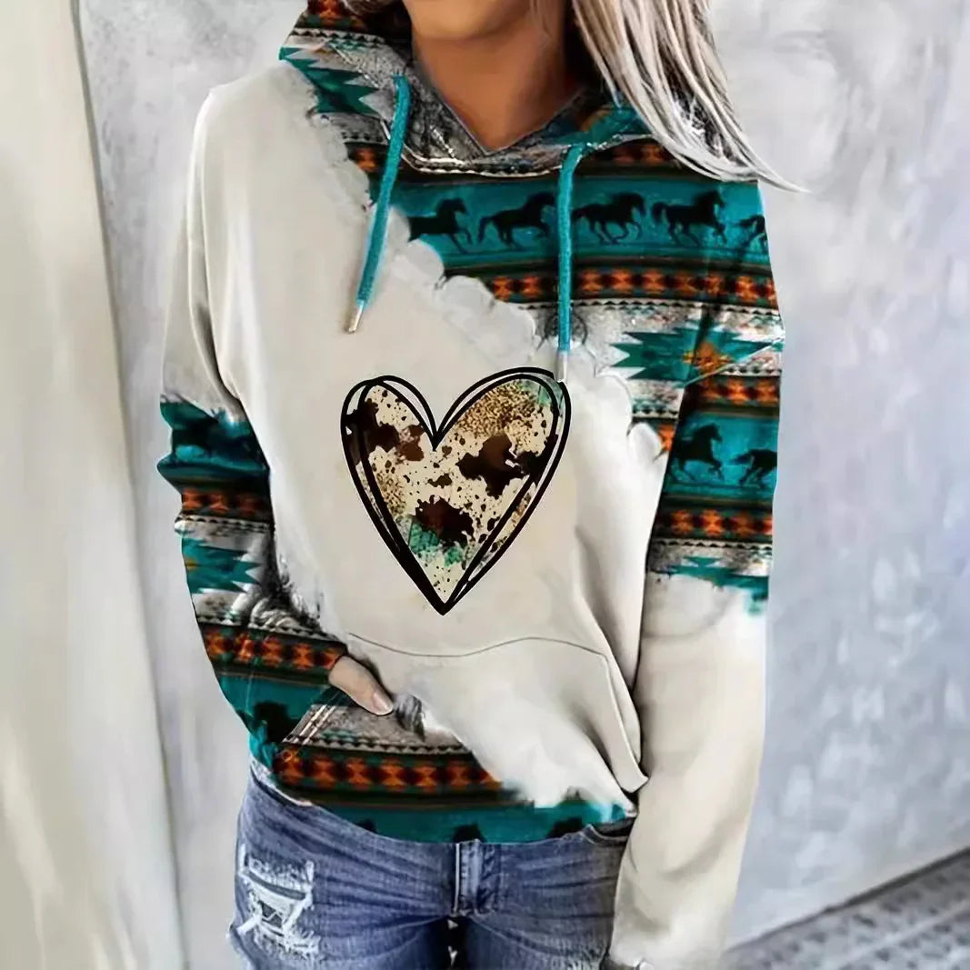 Woman wearing a beige hoodie with turquoise southwestern horse print and a large heart design, paired with ripped jeans