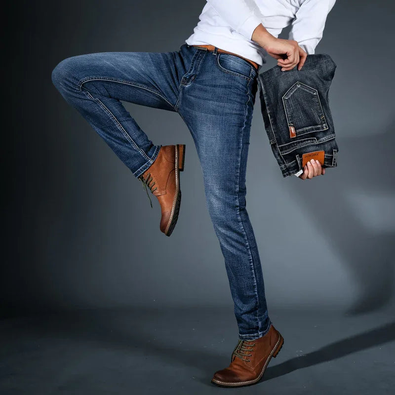 Man wearing slim fit blue jeans with brown leather boots holding folded dark denim pants