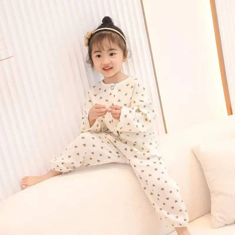 Happy toddler girl wearing cream pajamas with heart patterns sitting on white sofa in bright room
