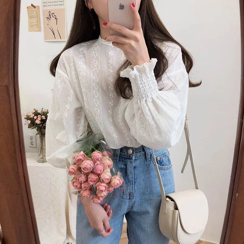 Woman wearing white lace blouse and blue jeans holding pink roses and beige crossbody bag