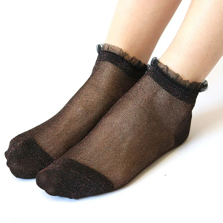 feet wearing black sheer ankle socks with ruffled edges on white background