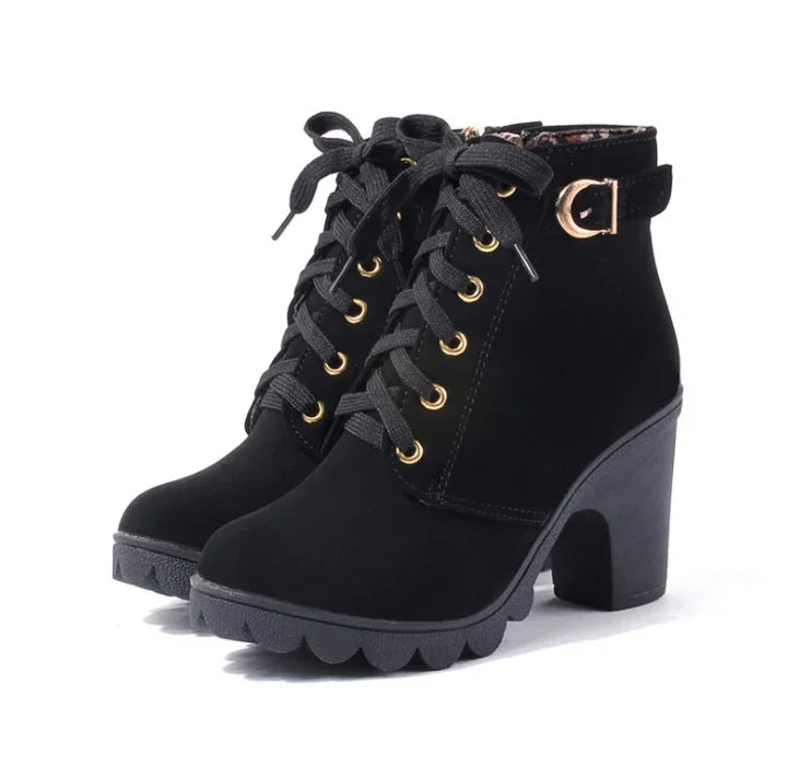 Black suede high-heeled ankle boots with gold eyelets, buckle detail, and rugged sole
