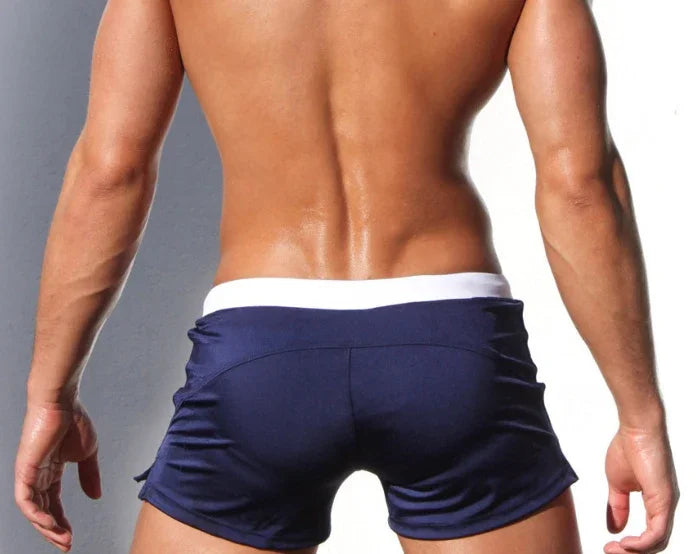Athletic man with muscular back wearing navy blue shorts and white waistband against grey background