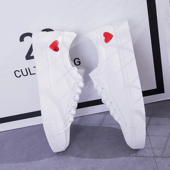 White canvas sneakers with red heart detail on the heel, displayed against a white and gray background