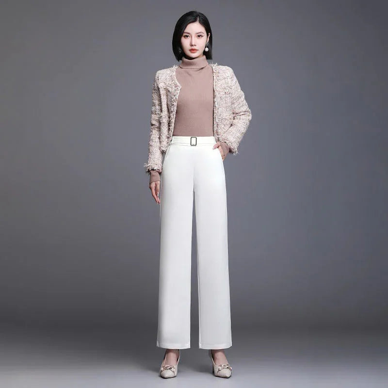 Woman in beige turtleneck sweater, textured jacket, white wide-leg pants, and beige heels against gray background