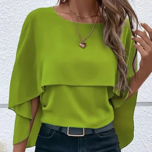 woman wearing lime green layered cape sleeve blouse with heart necklace and dark jeans