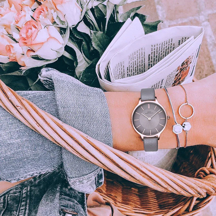 woman's wrist with gray leather watch and delicate bracelets holding basket with pink roses and newspaper