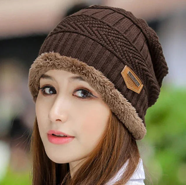 Young woman wearing a brown knit winter hat with faux fur trim and a leather brand patch