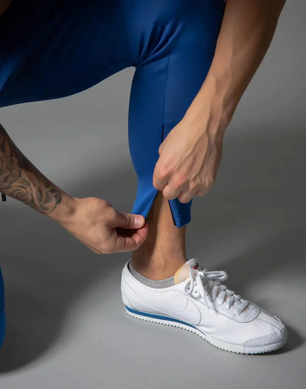 Person wearing blue athletic pants adjusting ankle zipper above white Nike Cortez sneakers