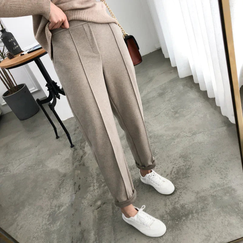 Woman wearing beige pleated pants with rolled cuffs and white sneakers in a modern room