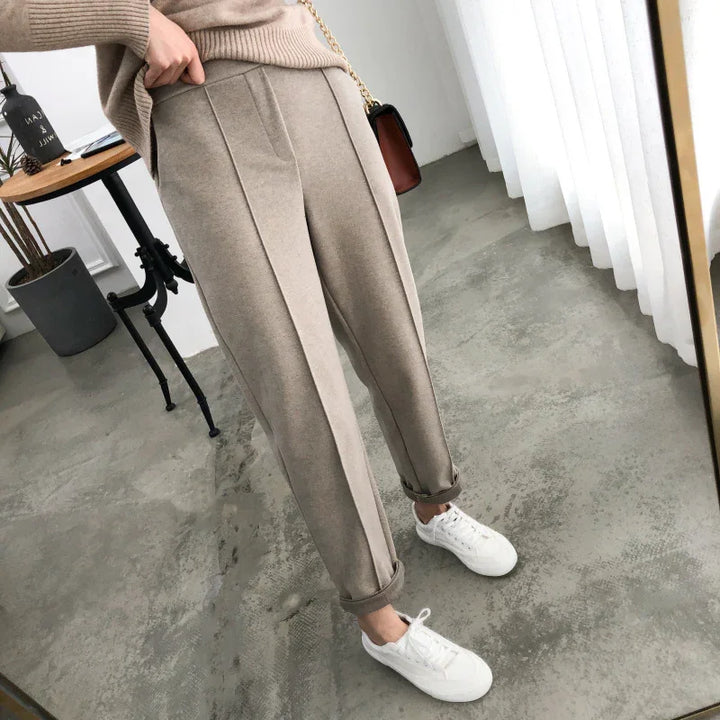 Woman wearing beige pleated pants with rolled cuffs and white sneakers in a modern room