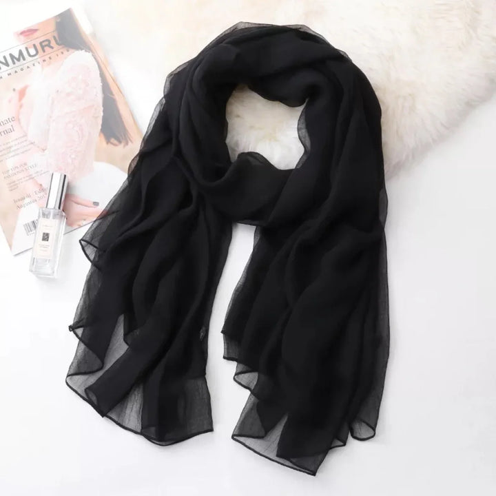 Lightweight black sheer scarf laid on white surface with fashion magazine and perfume bottle