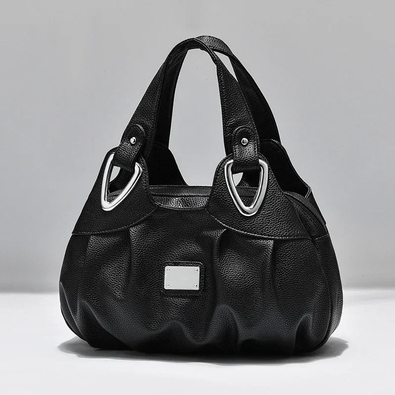 Black textured leather handbag with silver metal accents and short handles on white background