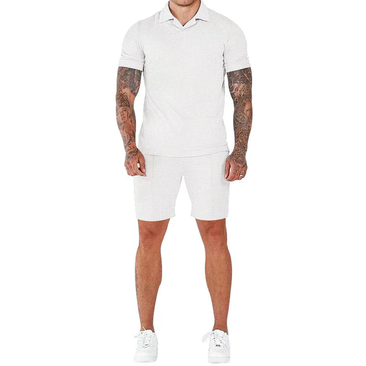 man with tattooed arms wearing white polo shirt, white shorts, and white sneakers