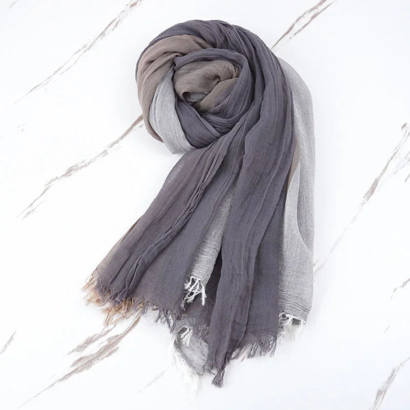 Soft gradient scarf in shades of gray and taupe with frayed edges on white marble background