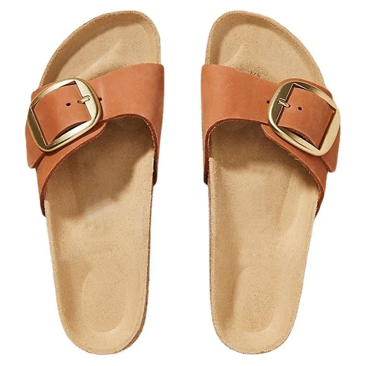 Pair of brown leather slide sandals with large gold buckle on beige footbed