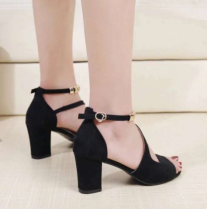 Black suede block heel sandals with ankle strap and gold buckle on model's feet