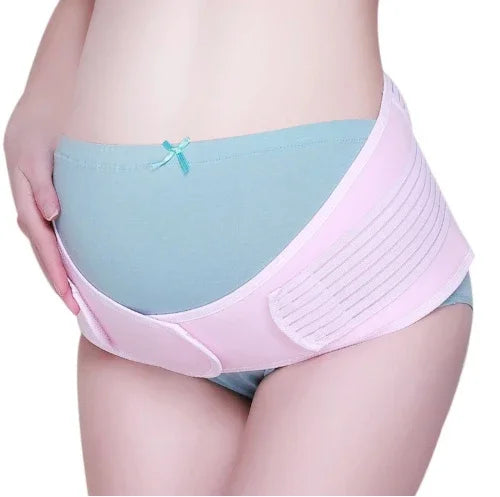 Pregnant woman wearing pink maternity support belt over teal underwear, hand resting on hip