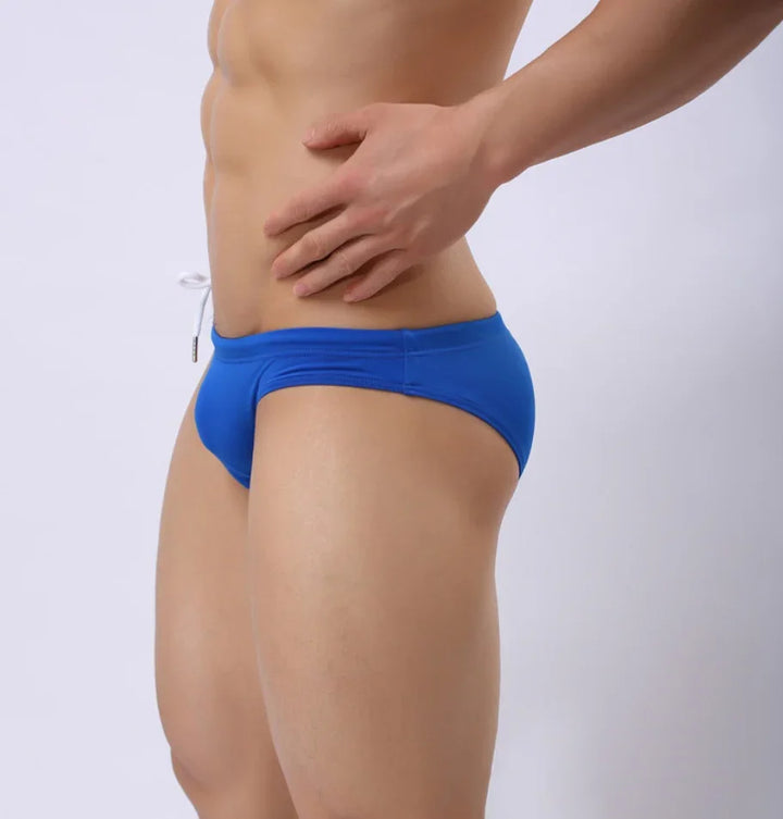 Male model wearing blue men's swim briefs posing against white background