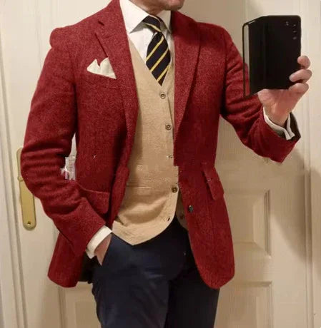 Man in red tweed blazer, beige vest, white shirt, striped tie, and navy pants taking a mirror selfie