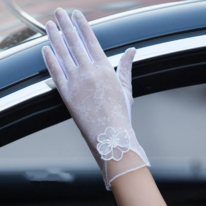 Hand wearing white lace glove with floral embroidery, resting on car window frame